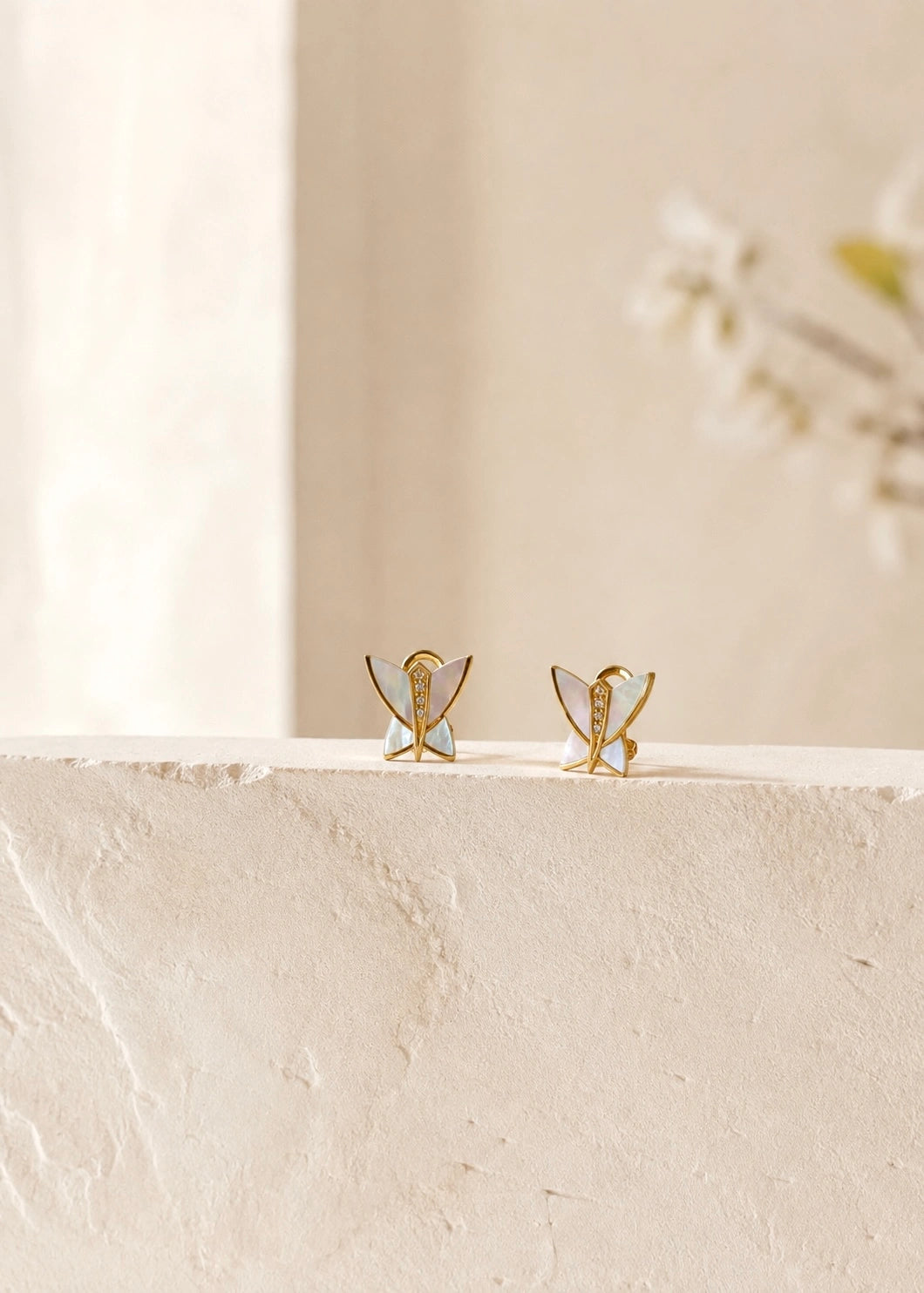 Close-up of a white mother of pearl butterfly earring worn on the ear