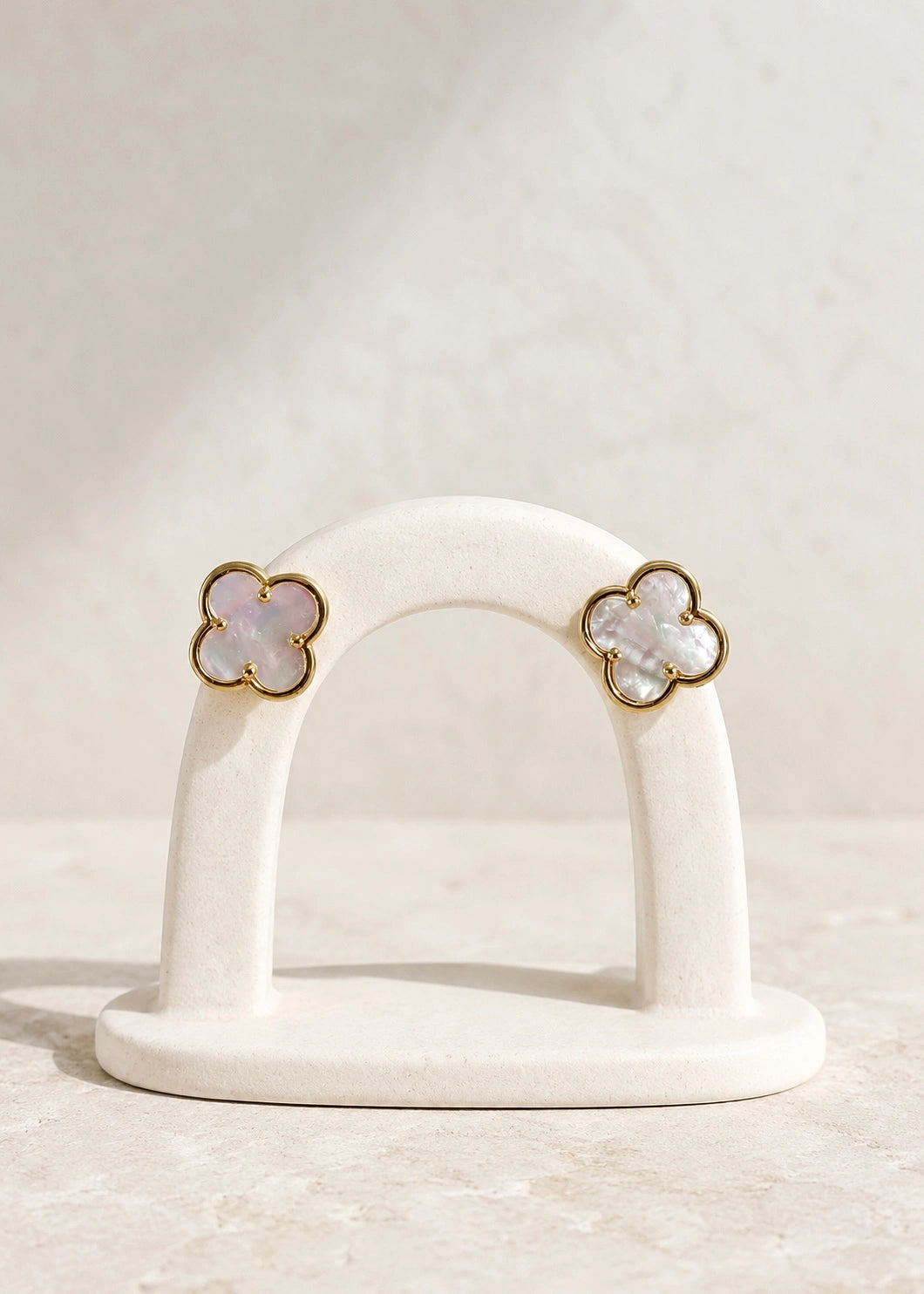 Natural mother of pearl four-leaf clover earrings on a display stand