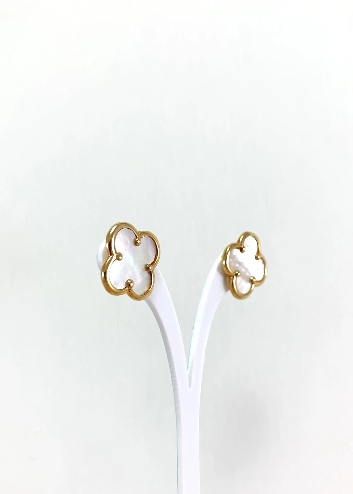 Pair of gold-plated four-leaf clover earrings with natural mother of pearl on a display stand