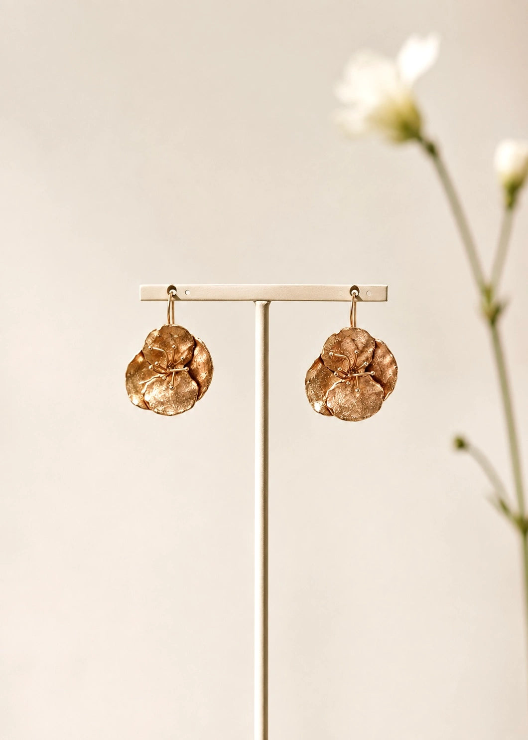 Pair of handmade bronze-tone flower earrings on a display stand