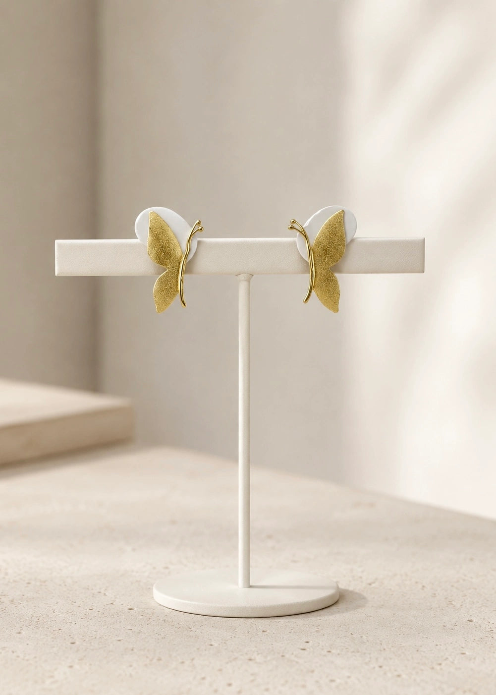 Pair of gold-plated butterfly earrings on a display stand
