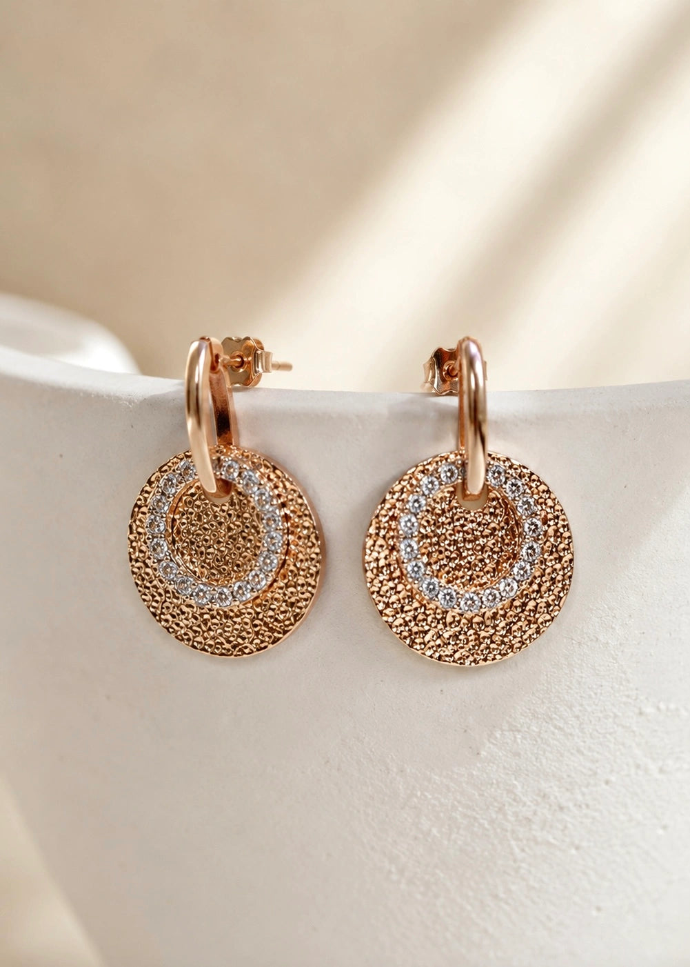 Bronze-tone earrings with a hammered disc and zircons on a display stand
