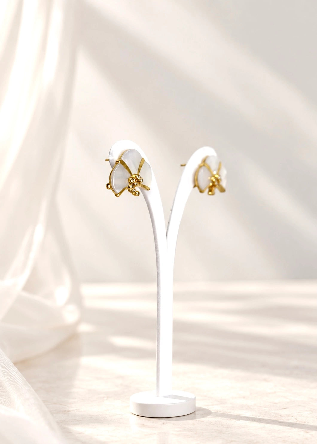Pair of white mother of pearl earrings with seven white zircons on a slim display stand