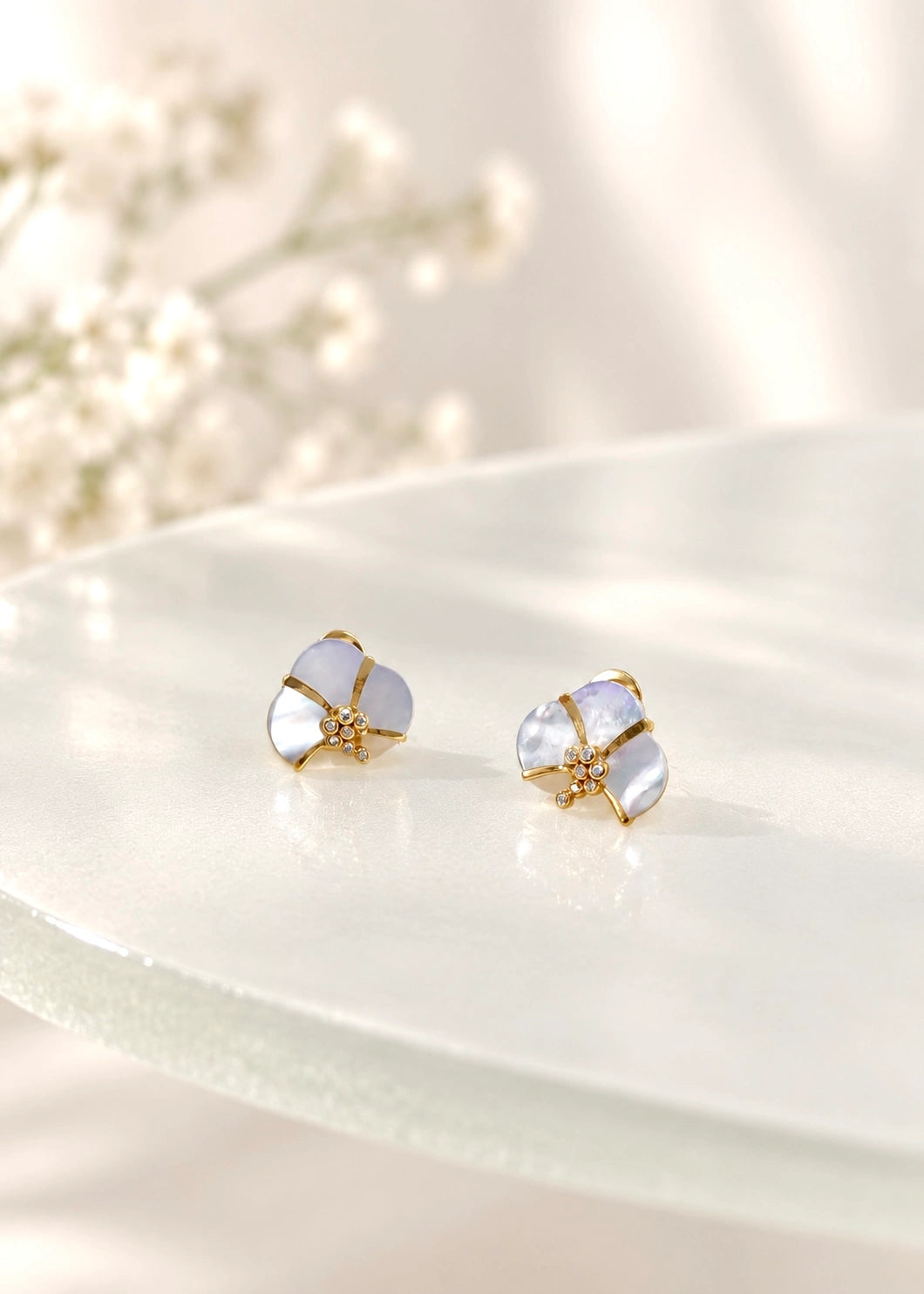 Close-up of a white mother of pearl earring with gold-plated lines and zircons worn on the ear